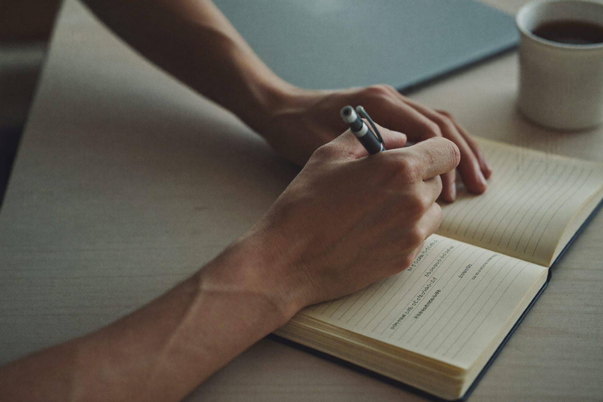 Hands, a notebook and a pen beside an open laptop