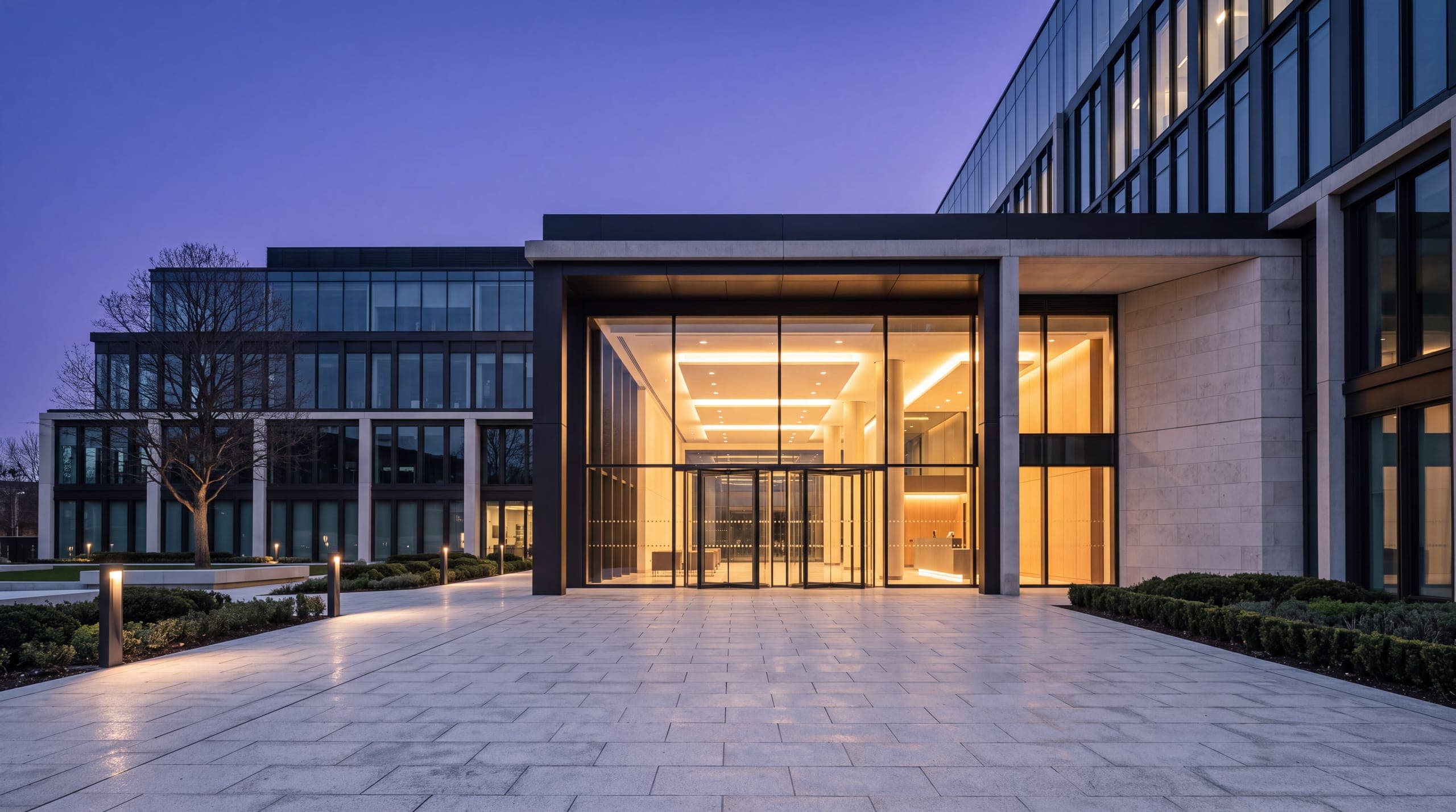 A lit building entrance across an empty plaza at dusk